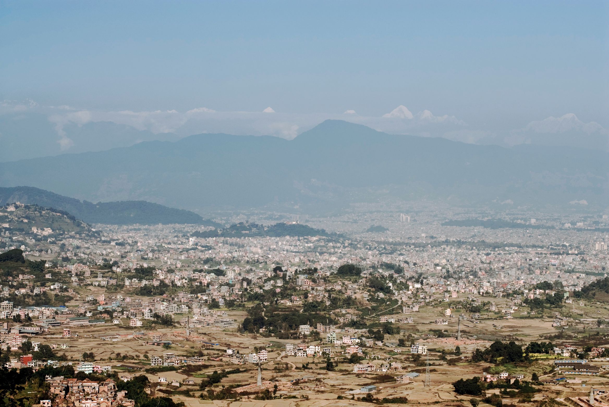 The city spread flat across the valley floor in the haze, ridges layered behind it