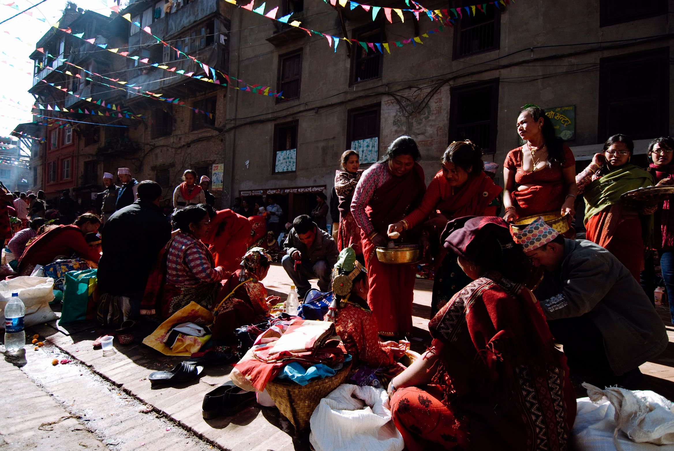 A crowd of women in red sitting out on the ground under bunting, food being handed round