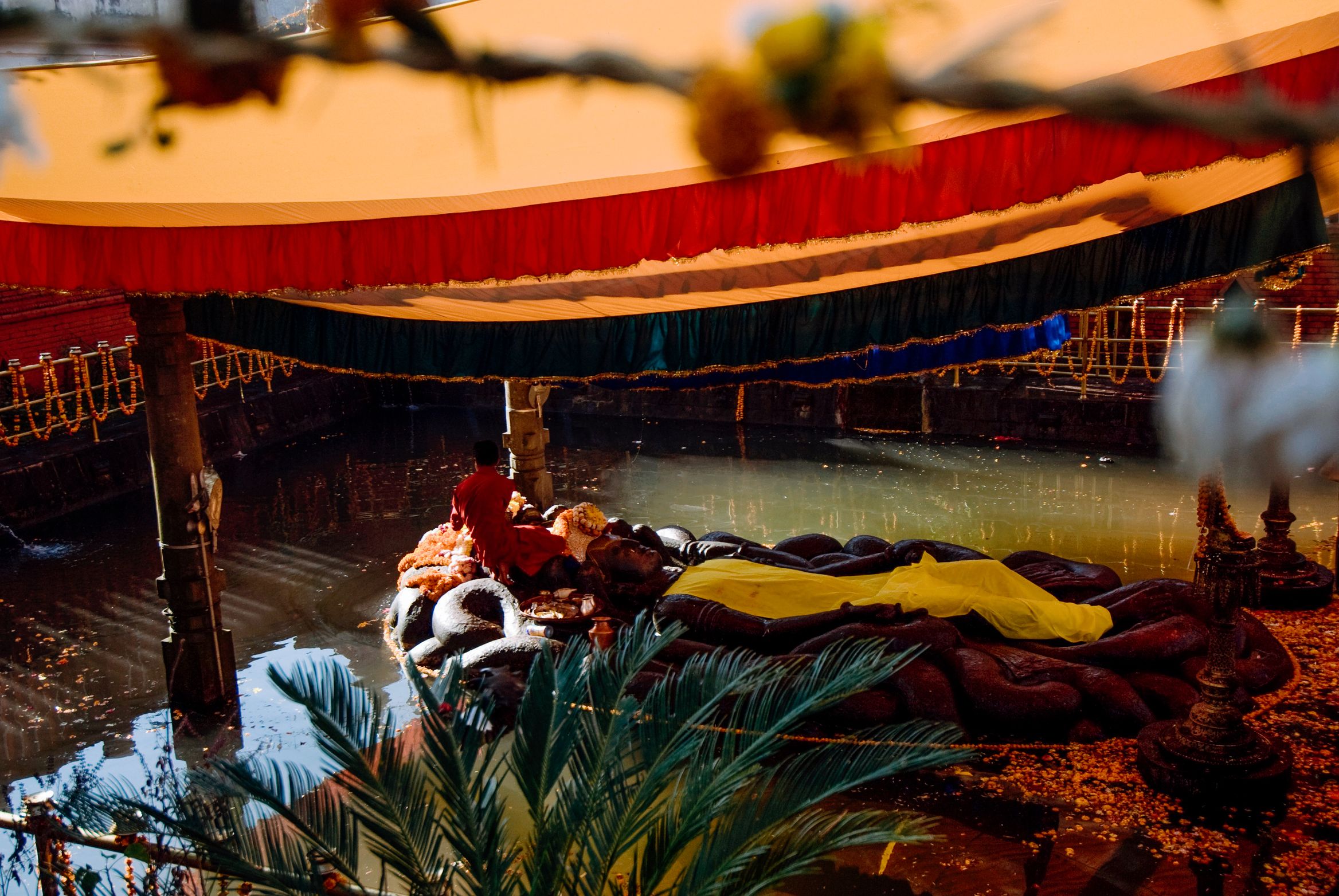 A striped canopy over a water tank, the reclining stone Vishnu heaped with cloth and flowers beneath it