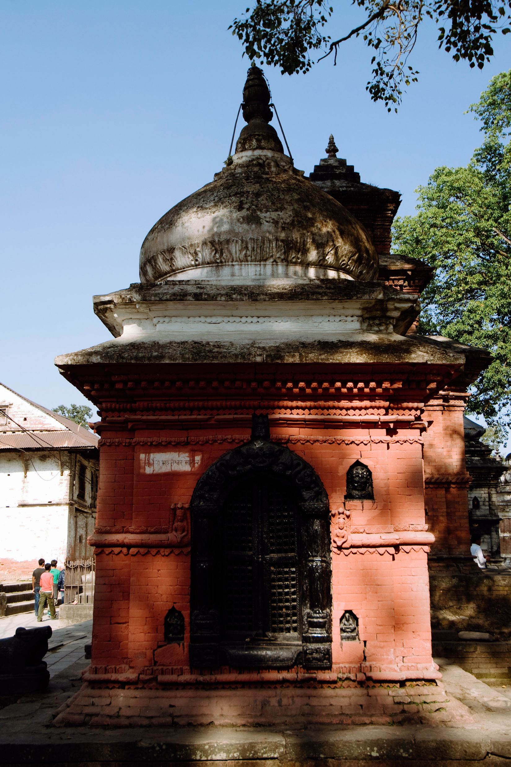 A shrine painted terracotta red with a blackened doorway and a dark dome above