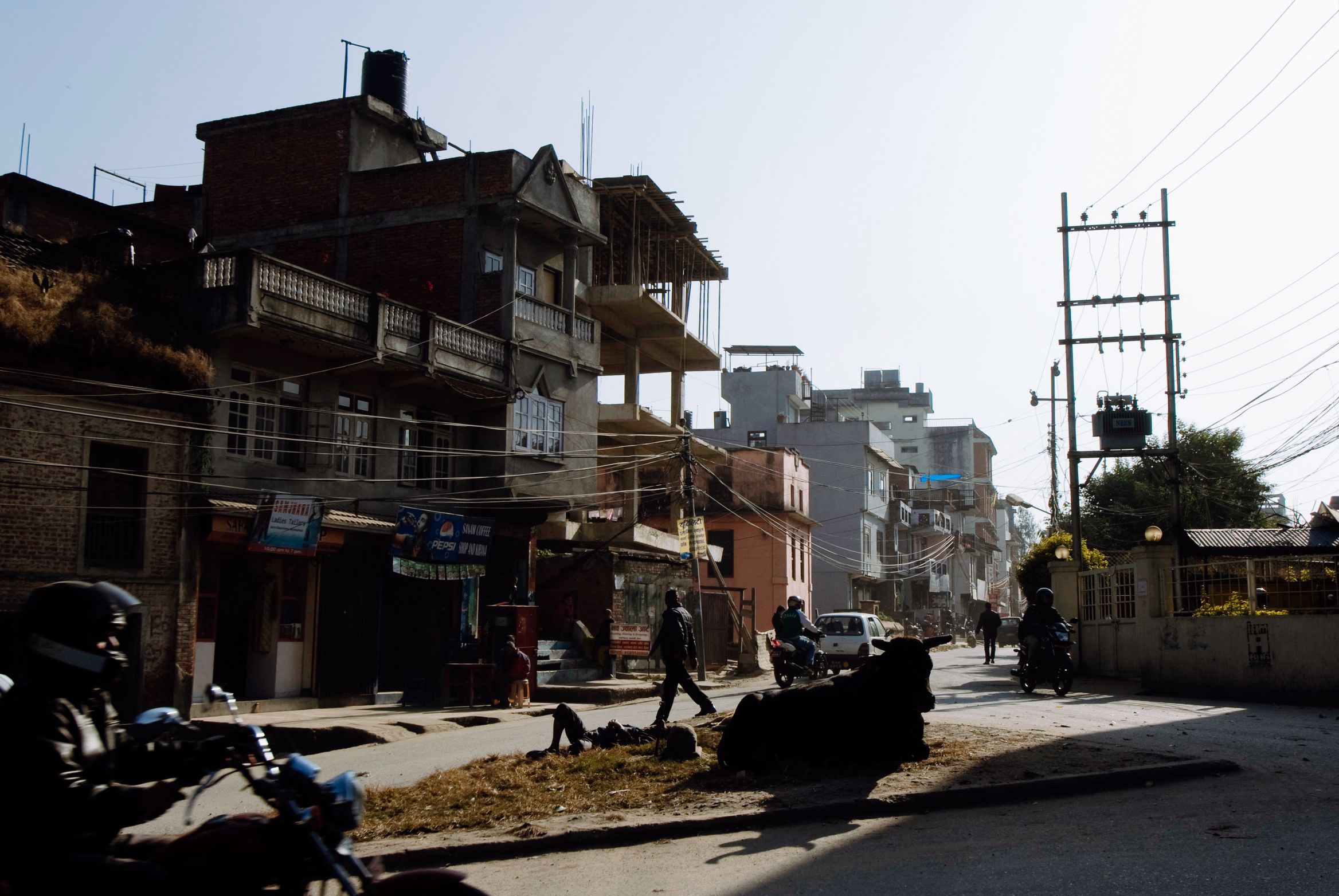 A street of concrete and brick buildings in low sun, motorbikes parked along the near side