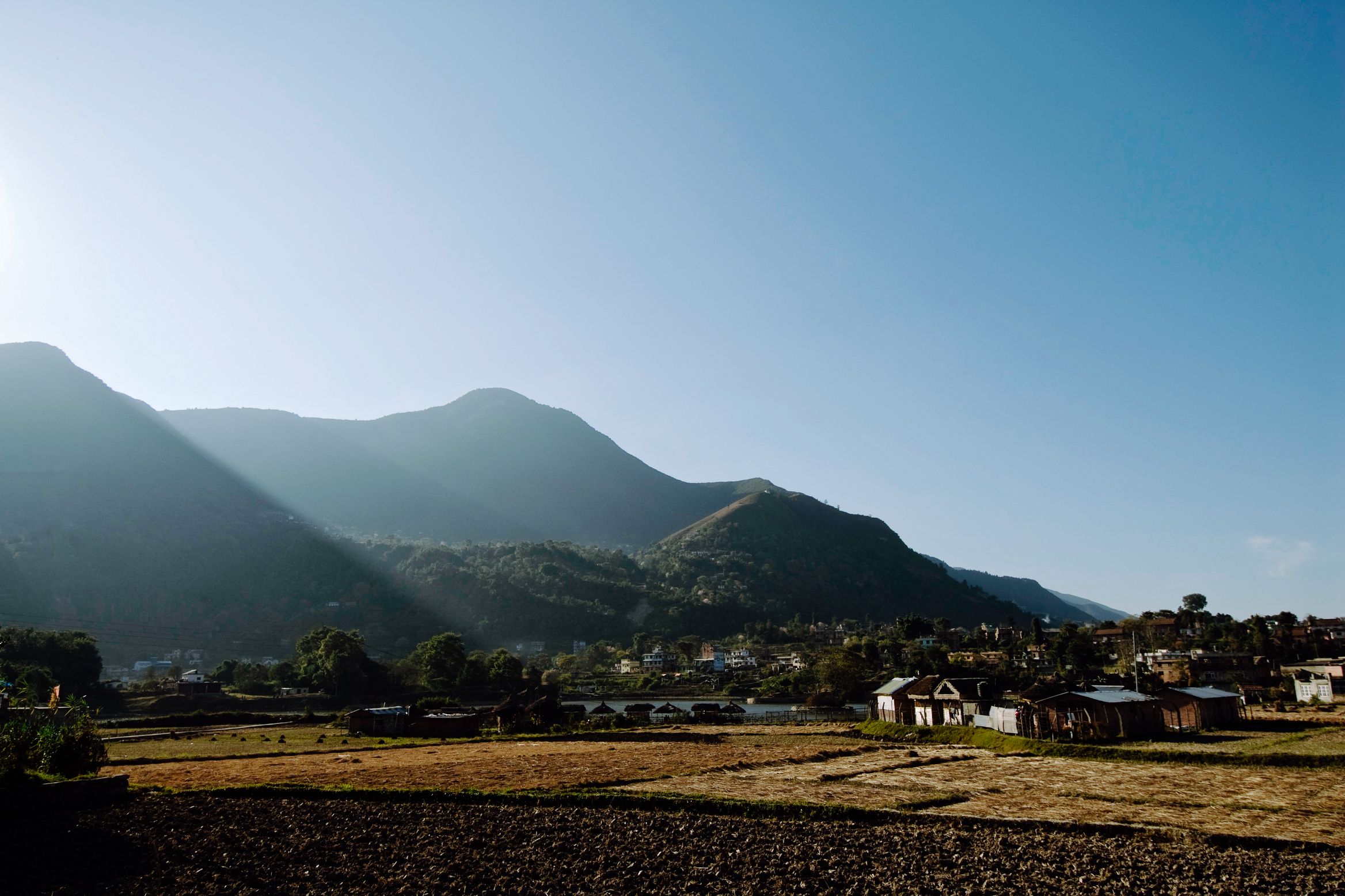 Ploughed fields in front of a village, the sun coming over a long dark ridge behind