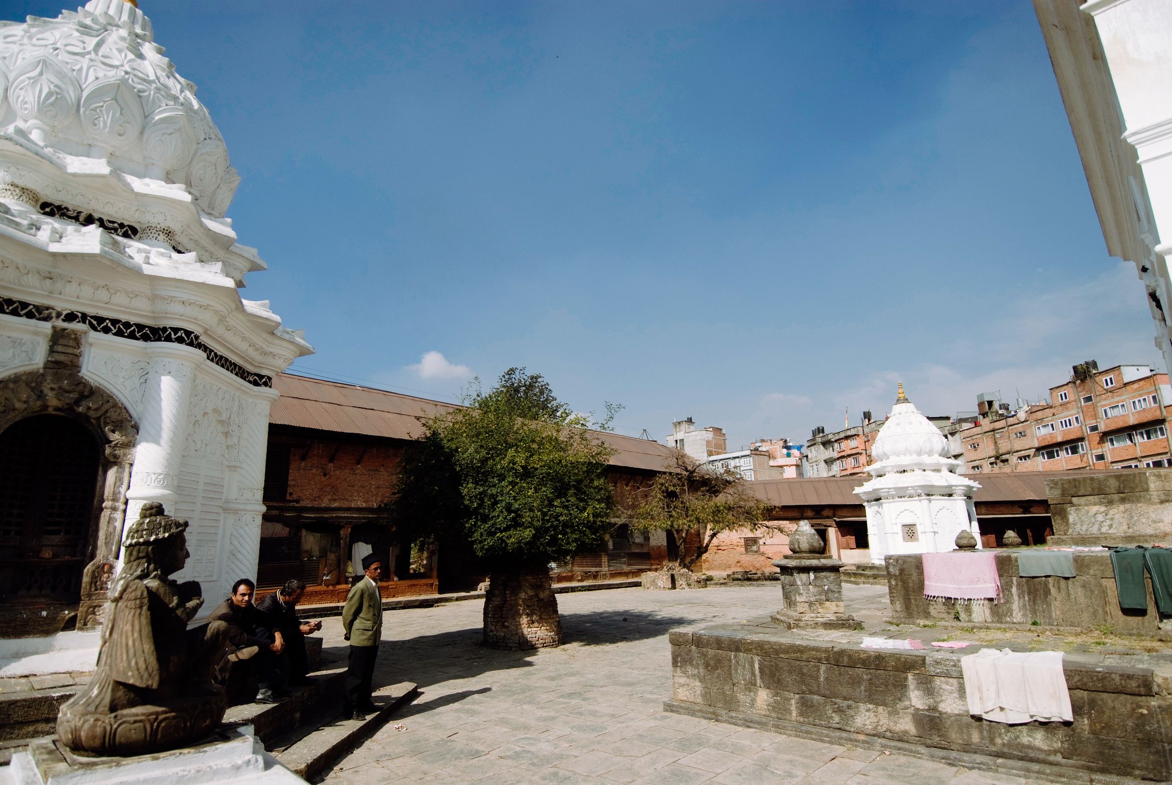 A quiet white temple courtyard, three men sitting talking on the plinth, washing laid out to dry