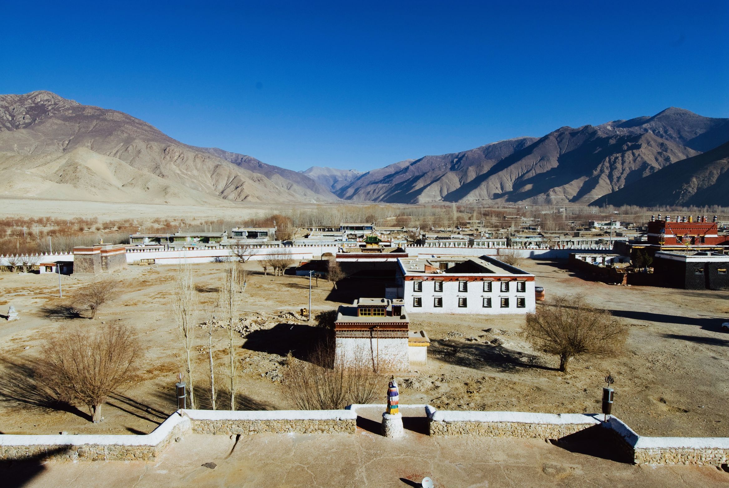 The monastery village spread across the valley floor, brown mountains rising behind