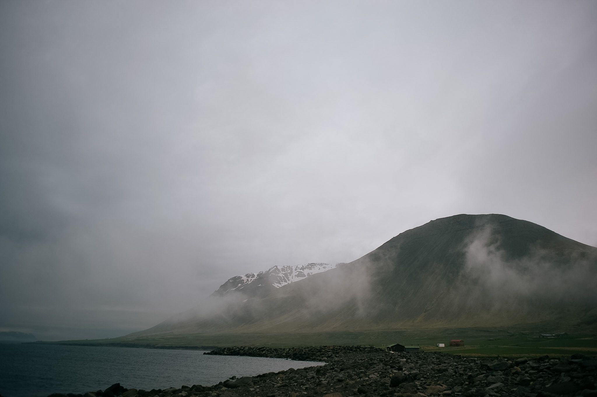 A green headland running down into the fjord, mist halfway up it and snow on the tops beyond