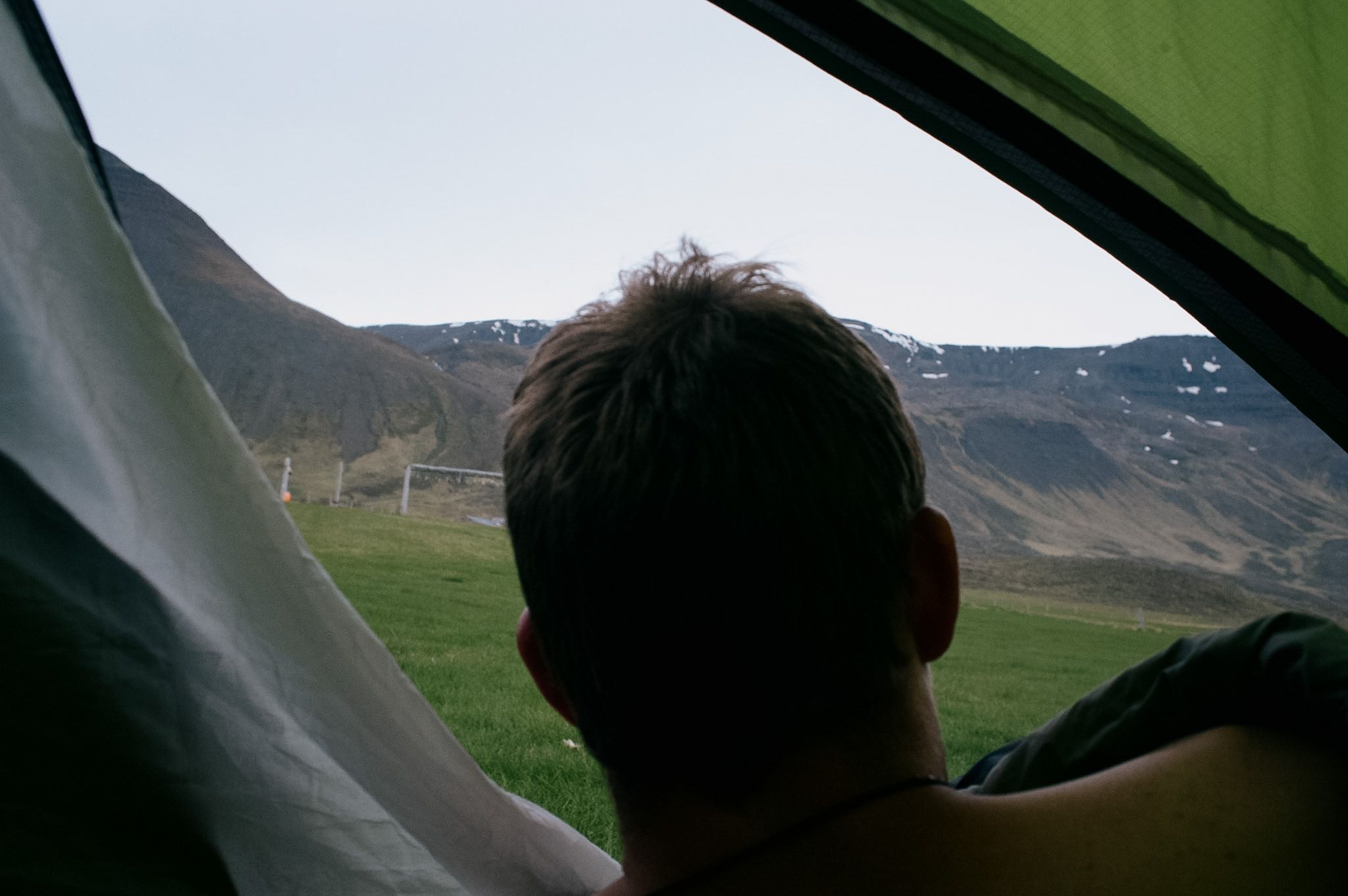 Looking out of a tent door past the back of someone’s head to a snow-streaked hillside in flat night light