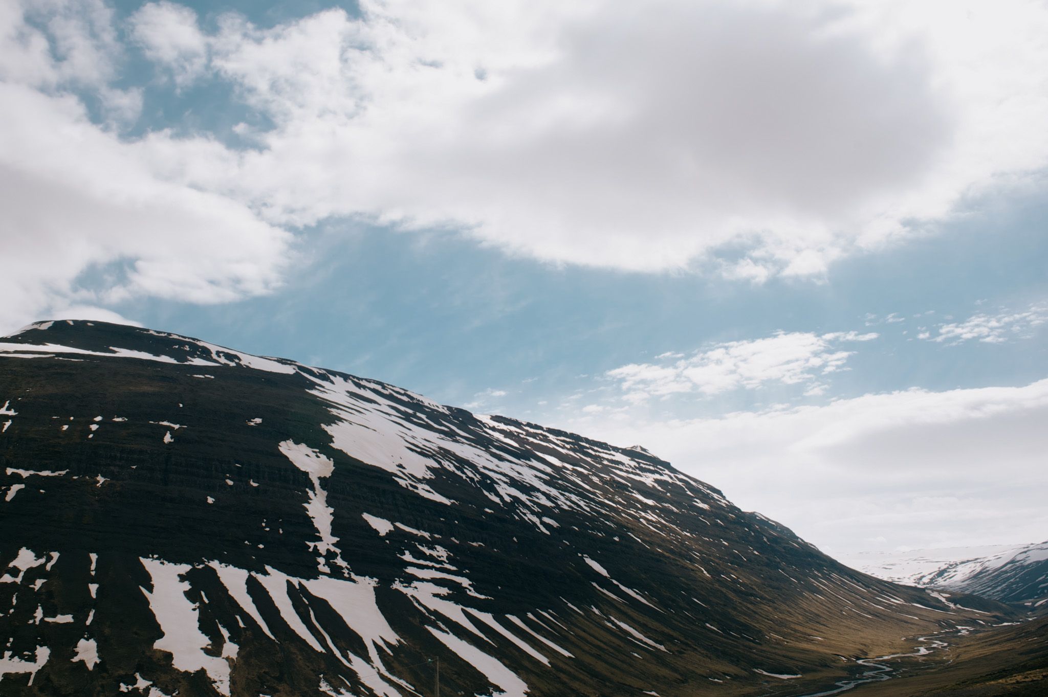 A long snow-streaked ridge falling away to a valley road, cloud breaking up over the top of it