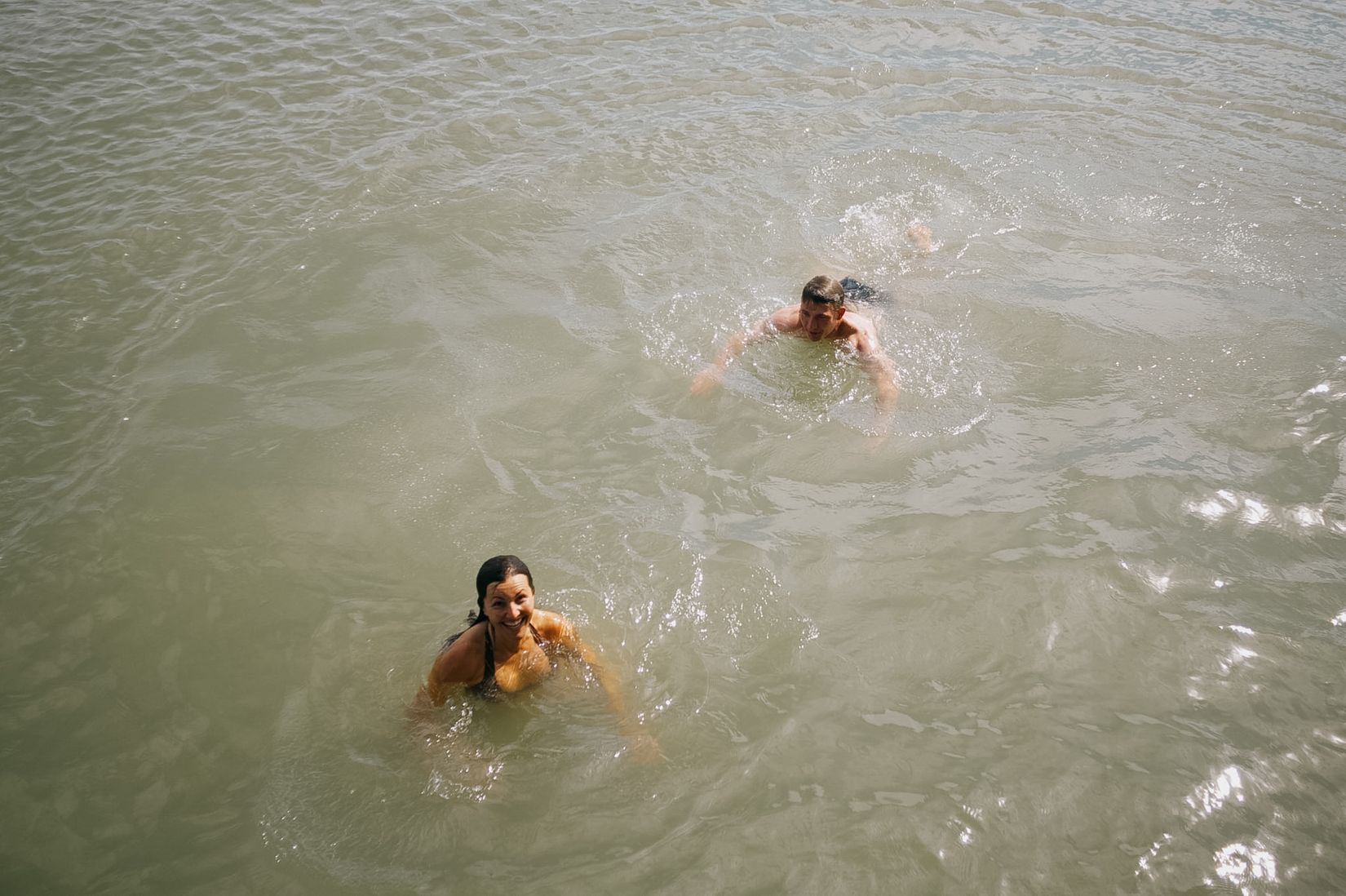 Two heads in green harbour water, both swimming back towards the wall