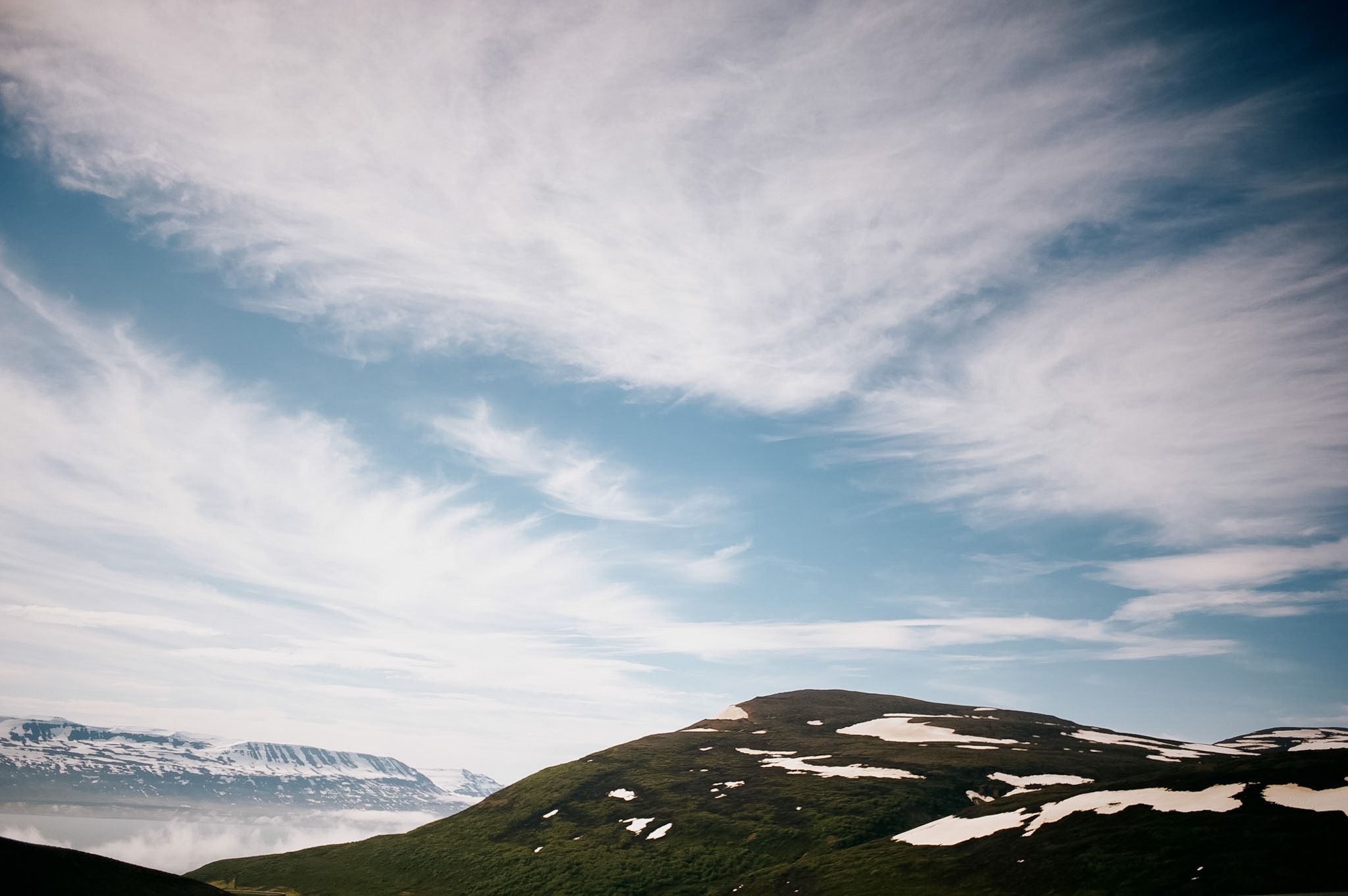 A bare rounded summit with snow in its hollows, high cloud fanning out above it