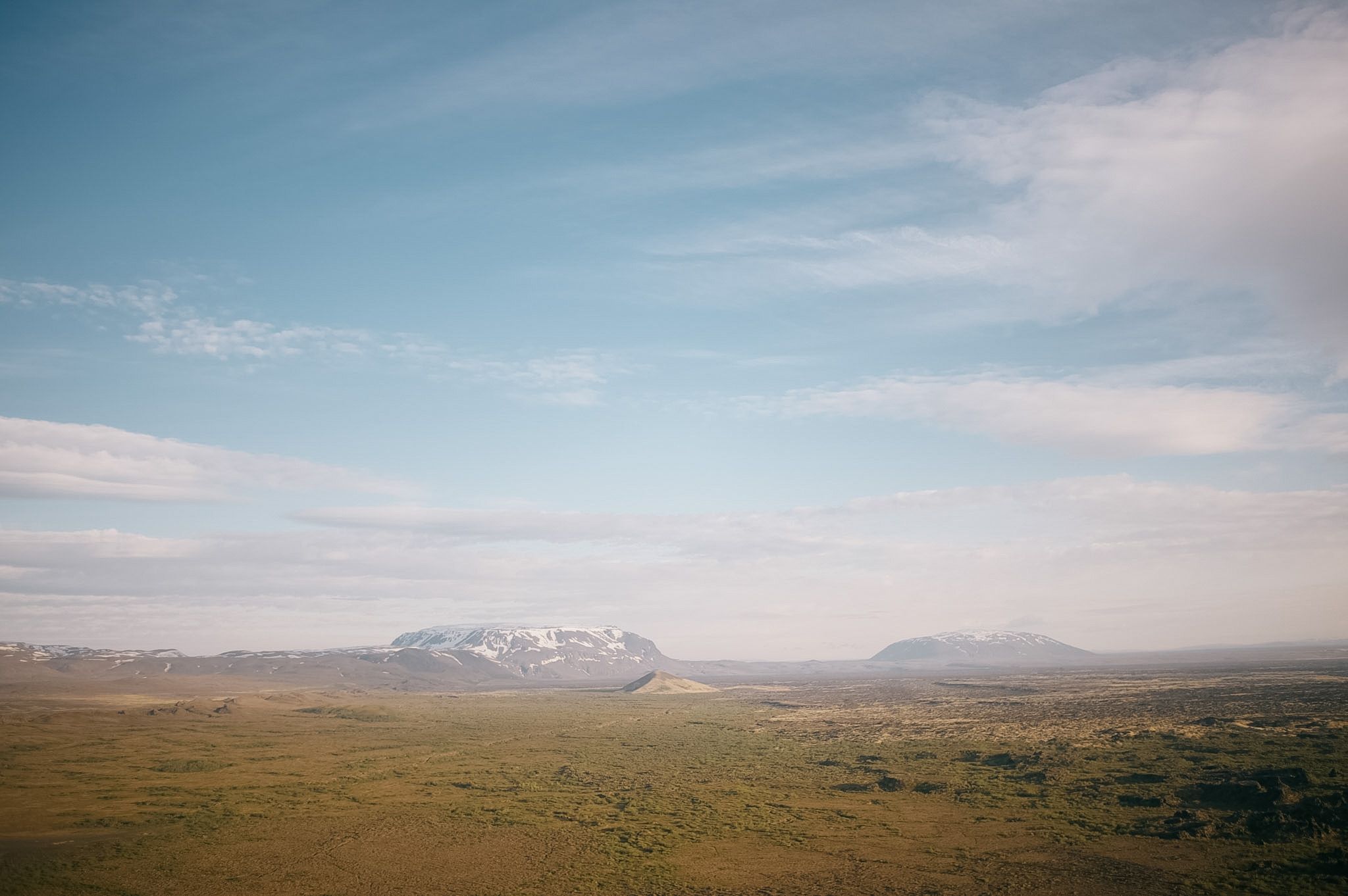 Two snow-capped table mountains standing out of a huge empty plain in the afternoon haze