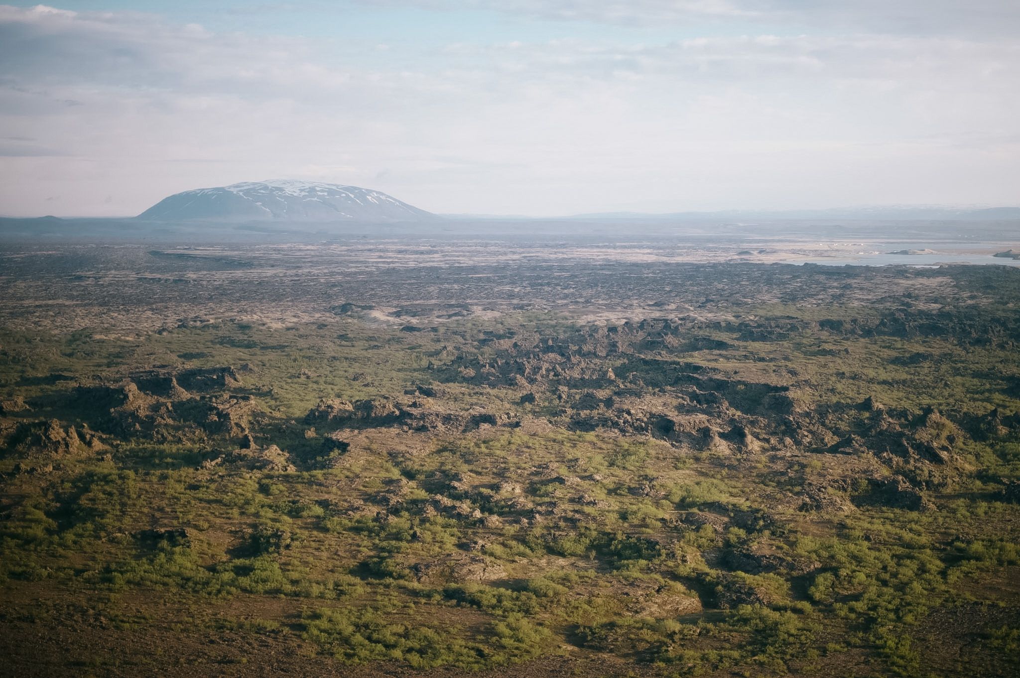 A broken lava field running to the horizon, moss softening the shapes, a white-topped dome behind