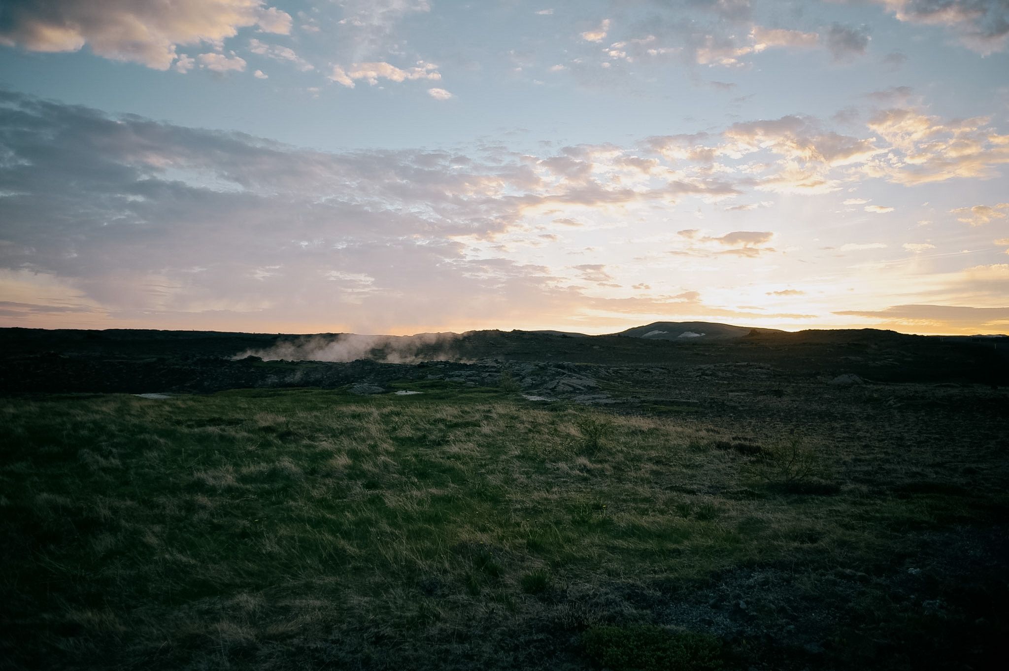 Steam drifting low over rough grass at sunset, the sky yellow behind a black ridge